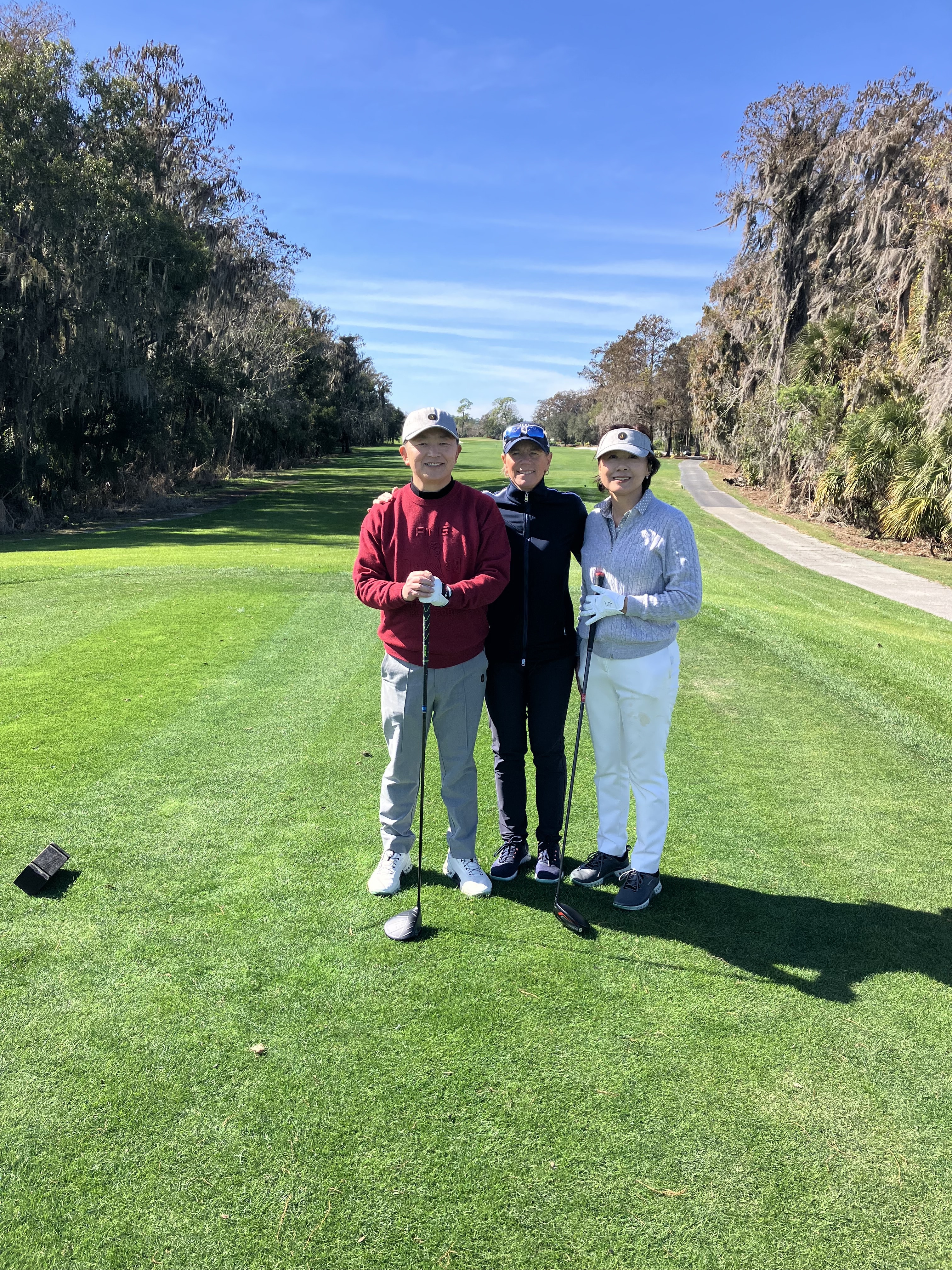 Three golfers with clubs on a tree-lined American course on a clear sunny day