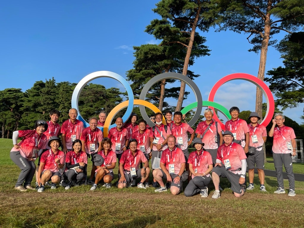 Large group in Tokyo 2020 Olympic shirts posing in front of the Olympic rings at the Olympic golf venue