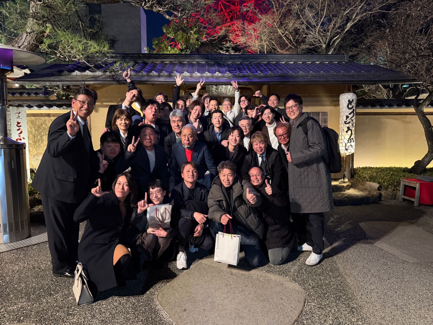 Large group celebrating outside a traditional Japanese restaurant at night with Tokyo Tower lit up in the background