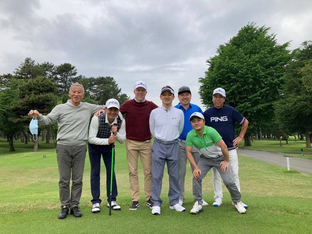 Seven golfers posing on a lush Japanese golf course on a cloudy summer day